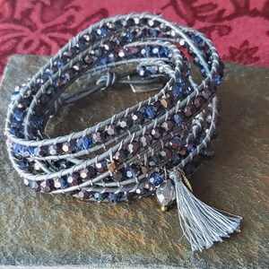 May include: A silver and blue wrap bracelet with a grey tassel. The bracelet is made of leather and beads.