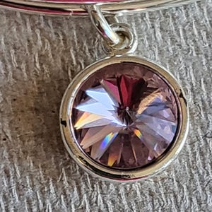 May include: A silver charm bracelet with a dangling charm featuring a light purple crystal.