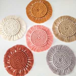 Peut inclure: Six sous-verres en crochet faits main dans différentes couleurs, dont le beige, le rose clair, la pêche et le brun. Chaque sous-verre présente un design circulaire avec une bordure en frange.