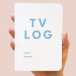 May include: A white notebook with rounded corners featuring the text TV LOG in large light blue letters. Below the title, there are two horizontal lines with the printed labels STARTED: and COMPLETED: for tracking television viewing progress.