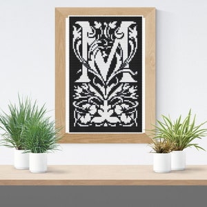 Könnte beinhalten: Ein gerahmtes Schwarzweiß-Kreuzstich-Design des Buchstabens "M" mit aufwendigen floralen Details.