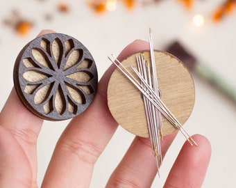 May include: Two wooden needle minders, one with a carved floral design and the other with a plain surface, holding needles.