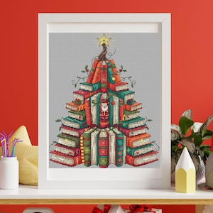 May include: A framed cross-stitch design of a Christmas tree made of books. The tree is composed of stacked books in various colours, with a Santa Claus figure in the centre. A gold star tops the tree, and the design is set against a grey background.
