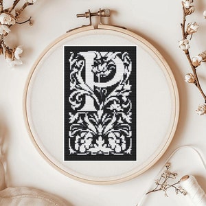 May include: Black and white embroidery hoop with a cross-stitch design of the letter "P" surrounded by intricate floral patterns.