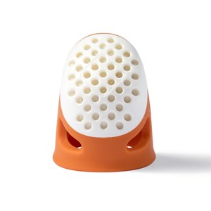 May include: Orange and white silicone thimble with a perforated top and a textured base.