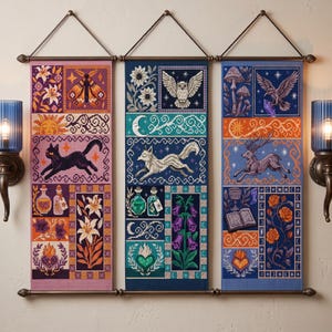 May include: Three vertical fabric wall hangings featuring detailed cross-stitch style illustrations. The panels display motifs including a moth, cat, owl, fox, deer, flowers, potions, books, and celestial symbols in vibrant purple, blue, and orange tones.