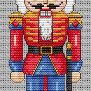 May include: A cross-stitch pattern of a traditional nutcracker soldier. The figure is dressed in a red jacket with gold accents, blue pants, and a black hat. It has a white beard and mustache, and is holding a black sword.