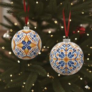 May include: Two white Christmas ornaments with intricate blue and yellow geometric patterns hang from red ribbons on a green Christmas tree. The ornaments have silver metal caps.