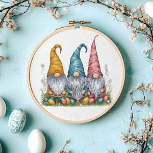 May include: Three gnomes sitting on a bed of green grass and surrounded by colorful Easter eggs. The gnomes are wearing yellow, blue, and pink hats and have white beards.