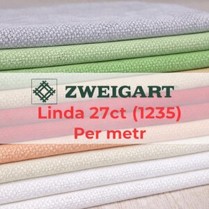 May include: A stack of Zweigart Linda 27ct fabric in various colors, including gray, green, pink, and cream. The fabric is neatly folded, showcasing its texture and color variations. The image includes the text "ZWEIGART Linda 27ct (1235) Per metr."