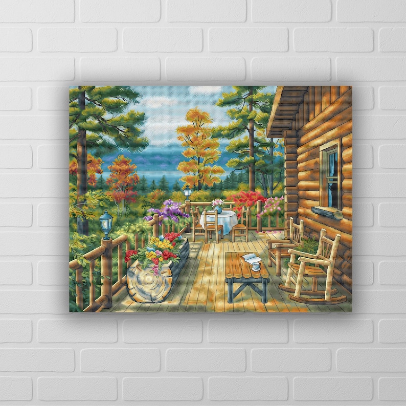 May include: A framed canvas print depicting a serene cabin scene. The artwork showcases a wooden deck with a table and chairs, a rocking chair, and vibrant flowers. The background features a lake and colorful trees.