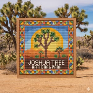 May include: A framed cross-stitch featuring a Joshua tree against a sunset. The text "JOSHUA TREE NATIONAL PARK" is displayed in brown. The frame is light brown, and the border has a colourful geometric pattern. The artwork is set in a desert landscape.