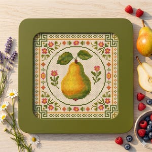 May include: A framed cross-stitch design featuring a yellow pear with green leaves, surrounded by floral and geometric patterns. The frame is a square shape with rounded corners and a green colour. The design is on a light beige background.
