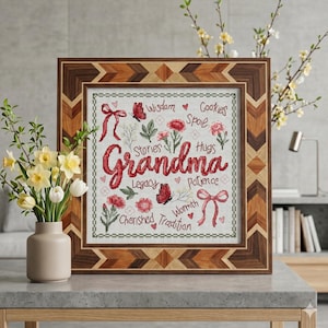 May include: A framed cross-stitch artwork with the word "Grandma" in red script. The artwork includes embroidered flowers, butterflies, and words like "Wisdom" and "Hugs." The frame has a geometric wood design.