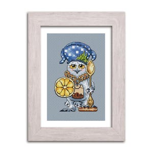 Puede incluir: Obra de arte en punto de cruz enmarcada de un búho con un gorro de dormir azul de lunares y sosteniendo una rodaja de limón y una cuchara. El búho tiene un collar y un pequeño tarro en el pecho. La obra está enmarcada en un marco de madera gris claro.