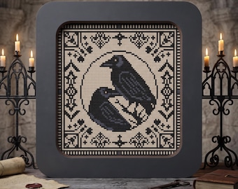 May include: A square framed cross-stitch embroidery featuring two black ravens centred within a circular border, surrounded by intricate black geometric patterns on a cream-coloured fabric background, encased in a dark grey rounded square frame.