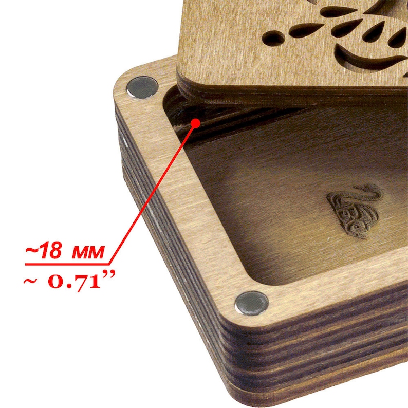 May include: Close-up of a wooden box with a hinged lid. The box is made of layered wood with a dark brown stain. The lid has a decorative cutout design. The box is approximately 0.71 inches deep.