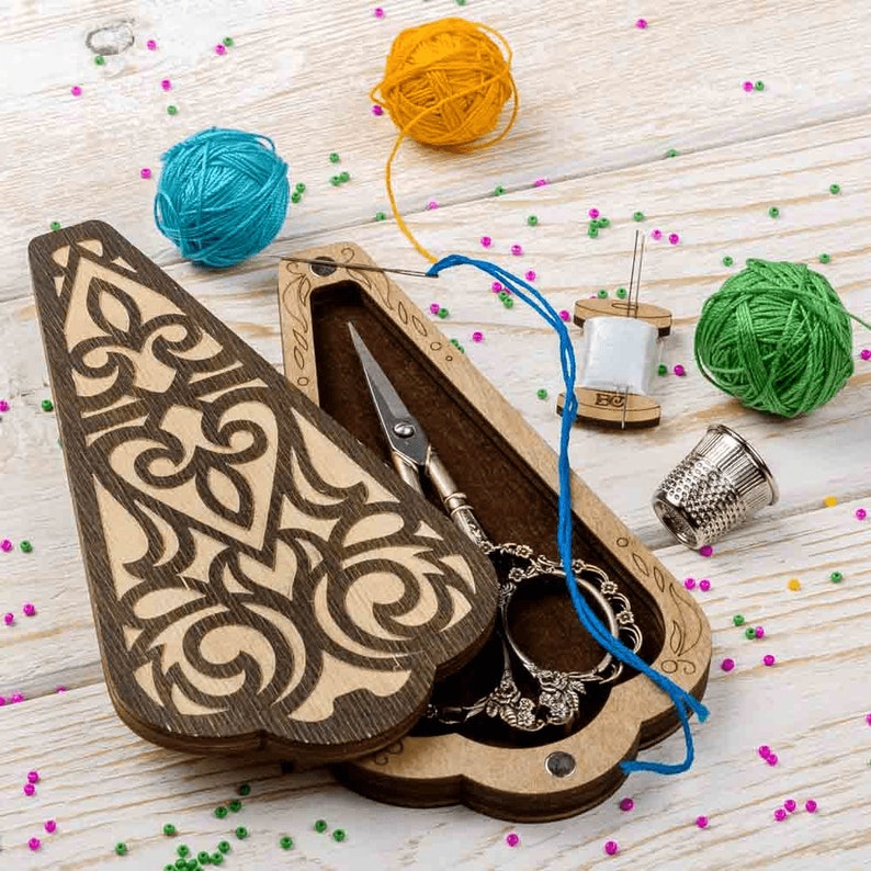 May include: A wooden sewing box with an intricate design, open to reveal a pair of scissors, a spool of thread, and a thimble. The box is surrounded by colorful yarn balls and beads.