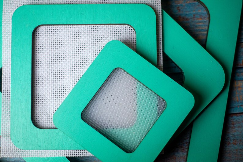 Op de afbeelding: Close-up van verschillende turquoise vierkante frames met afgeronde hoeken. De frames hebben een vensteruitsparing, die een witte, getextureerde stof onthult. De frames zijn gerangschikt in een gelaagde compositie.