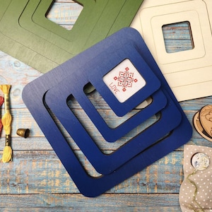 Op de afbeelding: Houten borduurringen in groen, blauw en cr&egrave;me, met een kruissteek met het woord "LOVE". Borduurgaren in rood en geel, een vingerhoed en een houten bloemenontwerp zijn ook aanwezig.