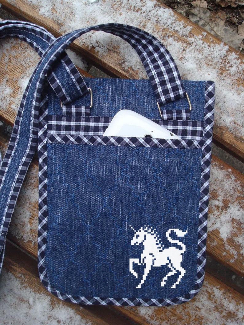May include: A blue denim crossbody bag with a white and black checked trim. The bag has a white embroidered unicorn design and a pocket for a phone.