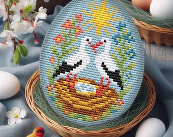 May include: An embroidered Easter egg featuring two storks in a nest, surrounded by flowers and a yellow sun. The egg is in a wicker basket with other eggs and flowers. The egg is approximately 5 inches tall.