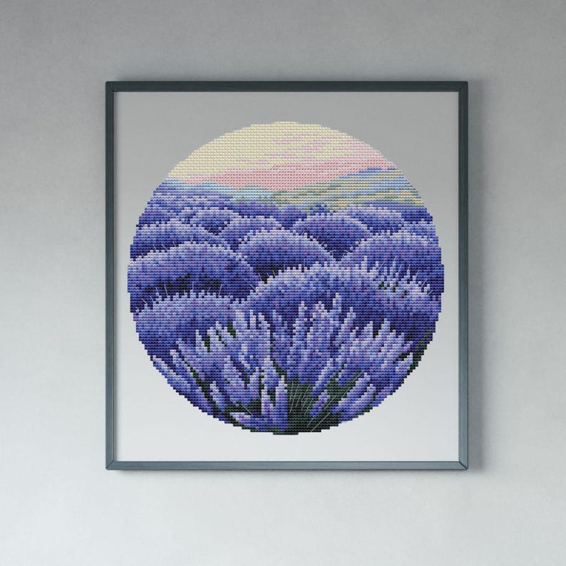May include: Framed cross-stitch art featuring a circular lavender field under a pastel sky. The artwork is dominated by shades of purple and green, with a light pink and yellow gradient at the top. The frame is a muted gray.