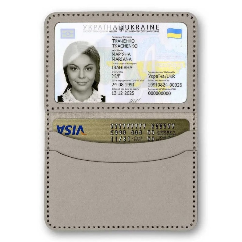 Op de afbeelding: Een grijze leren portemonnee met een transparant plastic venster dat een Oekra&iuml;ens paspoort met de naam "TKACHENKO MAR'YANA IBAHIBHA" en een VISA-creditcard in het onderste vakje toont.