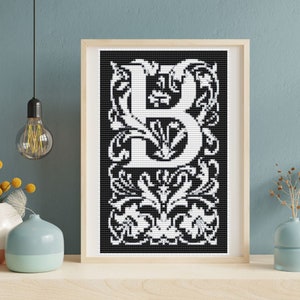 May include: A framed cross-stitch artwork featuring the letter "B" in white against a black background. The letter is designed in an ornate, floral style, with intricate details. The artwork is displayed in a light-colored wooden frame, adding a touch of elegance to the piece.