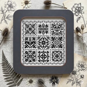 Peut inclure: Un échantillon de point de croix encadré avec une bordure grise. L'échantillon présente une grille de motifs géométriques et floraux noirs et blancs. Des fleurs séchées et des illustrations botaniques entourent le cadre, créant une esthétique vintage.