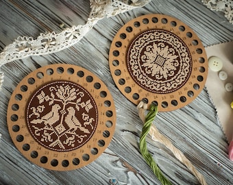 May include: Two circular wooden thread organizers with numbered holes around the perimeter. One features a cross-stitched bird and floral design, while the other displays a geometric star pattern. Strands of green and beige embroidery floss are attached.