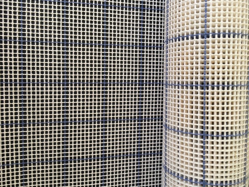 May include: A roll of white plastic canvas with blue grid lines. The canvas is used for needlepoint and other crafts.