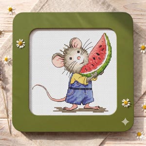 Op de afbeelding: Kruissteekkunstwerk van een lachende muis die een plak watermeloen vasthoudt. De muis draagt een blauwe overall en een geel shirt. Het kunstwerk is ingelijst in een groene vierkante lijst, met madeliefjes en lavendel in de achtergrond.