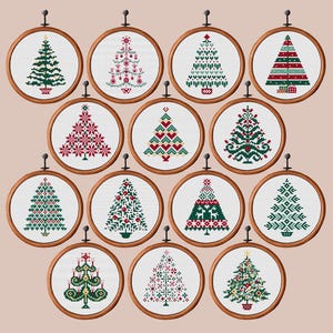 May include: A collection of 12 cross-stitch Christmas tree designs displayed in wooden embroidery hoops. Each tree features a unique pattern in shades of green, red, and white. The hoops are hung against a neutral background, showcasing the festive needlework.