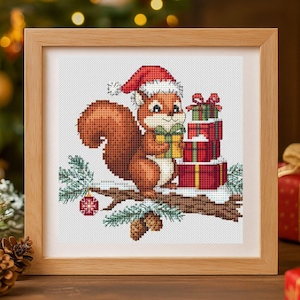 May include: A cross-stitch embroidery in a light wood frame depicting a brown squirrel wearing a red Santa hat, holding a yellow gift box, sitting on a snowy branch with pine cones, a red ornament, and a stack of red and green wrapped gifts.