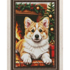 Könnte beinhalten: Ein gerahmtes Kreuzstichbild, das einen hellbraun-weißen Corgi-Hund zeigt, der auf einem Ziegelkamin liegt. Im Hintergrund sind ein Kamin mit brennendem Feuer, ein mit goldenen Kugeln geschmückter Weihnachtsbaum und eine grüne Girlande zu sehen.
