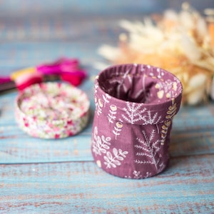 May include: A small, purple fabric storage container with a white floral pattern. The container is sitting on a blue wooden surface.