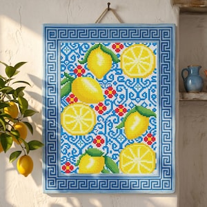 May include: A framed cross-stitch artwork featuring a lemon design. The artwork has a blue border with a Greek key pattern. The background is blue with white swirls and red flowers. Yellow lemons and lemon slices are the main focus.