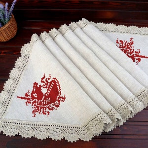 May include: A beige linen table runner with a crocheted border and two red embroidered unicorn designs.