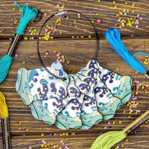 May include: A set of six wooden, blue and gold wave-patterned charms, strung on a black cord. The charms are shaped like a wave and have a white background with blue and gold waves.