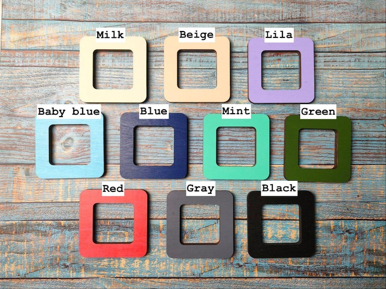 Op de afbeelding: Een verzameling van tien vierkante houten frames in verschillende kleuren, waaronder melk, beige, lila, babyblauw, blauw, mint, groen, rood, grijs en zwart. Elk frame heeft een vierkante uitsparing in het midden.