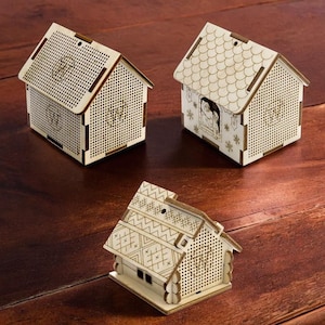 Könnte beinhalten: Drei Holzhäuser mit aufwendigen Designs und einer perforierten Oberfläche. Die Häuser sind aus hellem Holz gefertigt und haben einen rustikalen Charme.