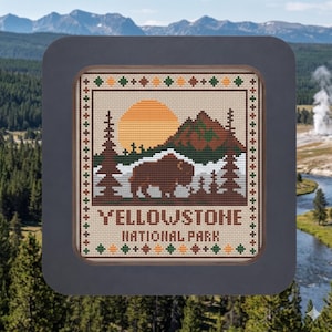 May include: Cross-stitch design featuring a bison, mountains, and a rising sun, with the text "YELLOWSTONE NATIONAL PARK." The design is framed in a dark gray square, set against a backdrop of a forest and mountains.