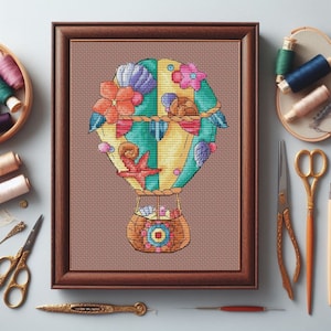 May include: A framed cross-stitch artwork depicts a colorful hot air balloon with a nautical theme. The balloon features seashells, starfish, and flowers in shades of orange, teal, and yellow. The basket is filled with shells, and the artwork is framed in a brown wooden frame.