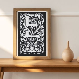 Könnte beinhalten: Ein gerahmtes Schwarzweiß-Kreuzstich-Design des Buchstabens "E" mit komplizierten Blumenmustern.