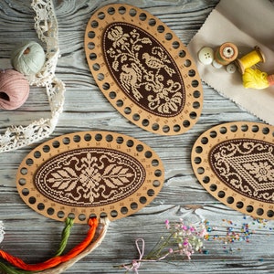 Pode incluir: Três aros de bordado de madeira de forma oval com desenhos de bordado castanho e bege. Os aros têm furos numerados ao redor das bordas. Também há carretéis de fio e lã em várias cores.