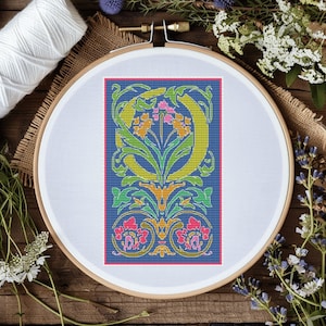 May include: A cross-stitch pattern featuring a stylized letter 'O' surrounded by floral motifs in shades of green, yellow, orange, pink, and blue on a dark blue background.