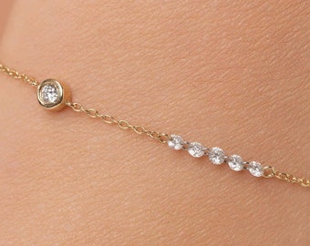 May include: A delicate gold chain bracelet with a single round diamond at the center and a row of smaller diamonds along the bottom.