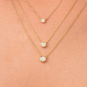 May include: Three gold necklaces with small round clear stones hanging from them. The necklaces are layered on a person's neck.