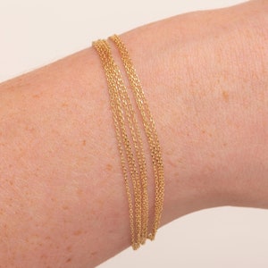 May include: A gold chain bracelet with multiple strands, worn on a person's wrist.